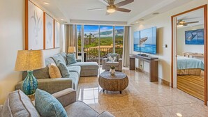 A modern living room with a sofa, armchair, round coffee table, and a television. - Where Haleakala Meets the Sea Kihei Remodeled Oceanfront Condo Rooftop BBQ (Kihei)