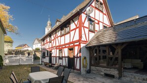 Une maison traditionnelle à colombages, avec un escalier en pierre, une clôture blanche et une table avec des chaises à l’extérieur.