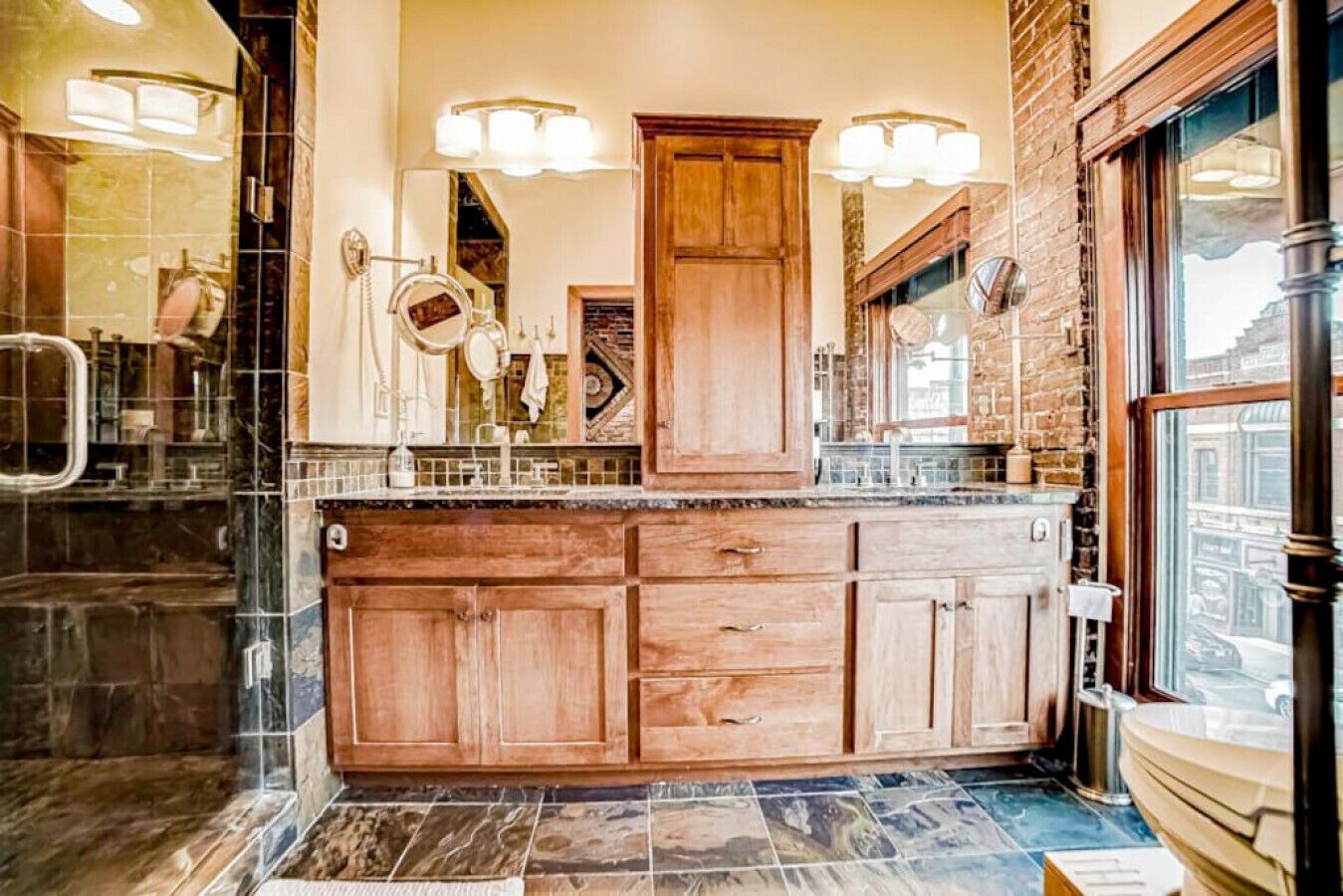 Une salle de bain avec un meuble-lavabo en bois, des carreaux de marbre et un grand miroir avec éclairage intégré.