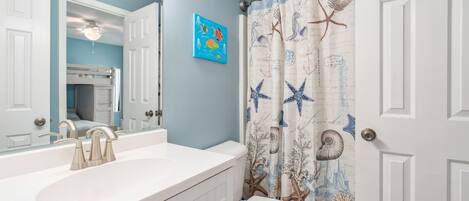 Een badkamer met een wit wastafel, een spiegel en een toilet. De muur is blauw en er is een douchegordijn met een nautisch thema.