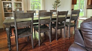 A dining area with a wooden table and chairs, a bookshelf, and a window with curtains. - Name: Hill Crest<br>Private Setting. Heated Pool. 4 Minutes to Dreams Park  (Cooperstown)