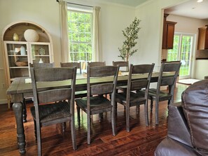 A dining area with a wooden table and chairs, a bookshelf, and a window with curtains.