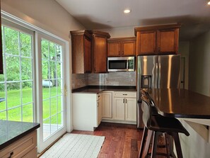 A kitchen with wooden cabinets, a stainless steel refrigerator, a microwave, and a large window.