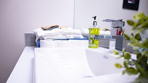 A bathroom with a white sink, a bottle of yellow liquid soap, and neatly folded towels. - Exquisite & Cozy La'Posh Suite w/WiFi, Workspace, Storage (Airdrie)