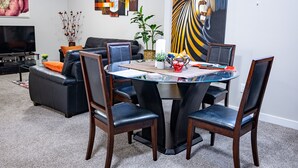 A modern living room with a black leather sofa, a glass-top dining table surrounded by wooden chairs, and a large abstract painting on the wall. - Exquisite & Cozy La'Posh Suite w/WiFi, Workspace, Storage (Airdrie)