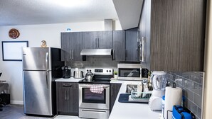 A modern kitchen with stainless steel appliances, grey cabinetry, and a tiled backsplash. - Exquisite & Cozy La'Posh Suite w/WiFi, Workspace, Storage (Airdrie)