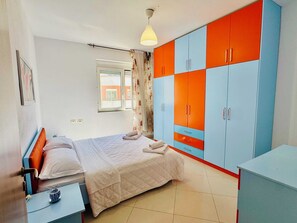 Een slaapkamer met een bed, nachtkastje, kledingkast en een raam met gordijnen.