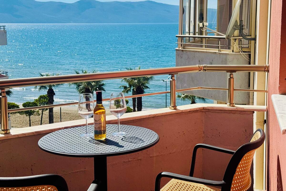 A balcony with a table and chairs, overlooking a beach and the sea.