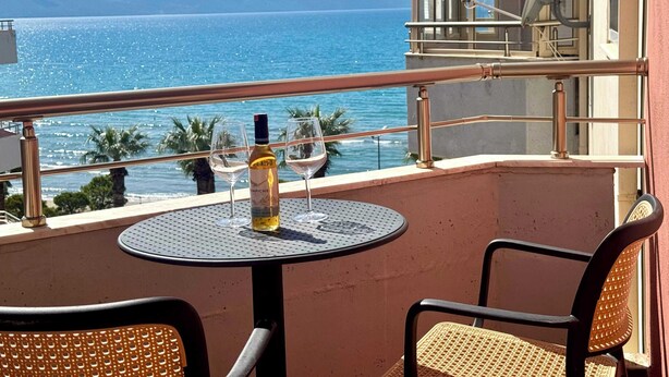Ein Balkon mit Tisch und zwei Stühlen mit Blick auf ein Gewässer und Palmen.