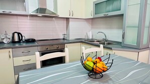 Eine moderne Küche mit weißen Schränken, einer Edelstahl-Dunstabzugshaube, einem Spülbecken und einer Obstschale auf der Arbeitsfläche.