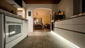 A modern kitchen with a built-in oven, a dining area with a table and chairs, and a view into the living room.