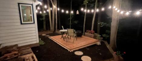A backyard with a wooden deck, a table and chairs, and string lights.