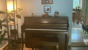 Un pianoforte in una stanza con pavimento in legno, una lampada da terra e un quadro appeso al muro.