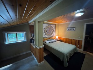 Um quarto com uma cama, uma janela, um tapeçário e uma porta que dá para outro cômodo.