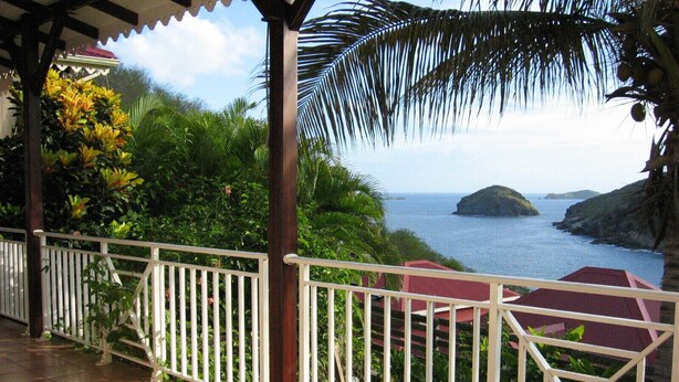 A covered outdoor area with a tiled floor, white railings, and a view of the ocean and a small island. - Villa COLORADO - GdF - ANSE FIGUIER (TERRE DE HAUT)