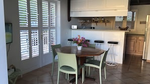 A dining area with a wooden table and chairs, a flower vase, and a kitchen in the background. - Villa COLORADO - GdF - ANSE FIGUIER (TERRE DE HAUT)