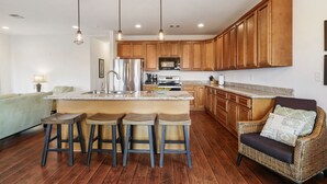 A modern kitchen with wooden cabinets, a stainless steel refrigerator, a microwave, and a central island with bar stools.