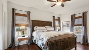 A bedroom with a wooden bed, a nightstand, a ceiling fan, and a window with curtains.