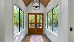 A hallway with wooden floors, large windows, and a double door.