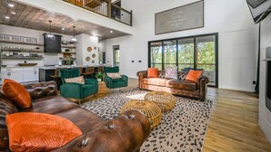 A spacious living area with a high ceiling, a cozy seating arrangement, and a view of the outdoors.
