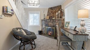 Una sala de estar acogedora con chimenea de piedra, un sillón cómodo y un escritorio de madera.