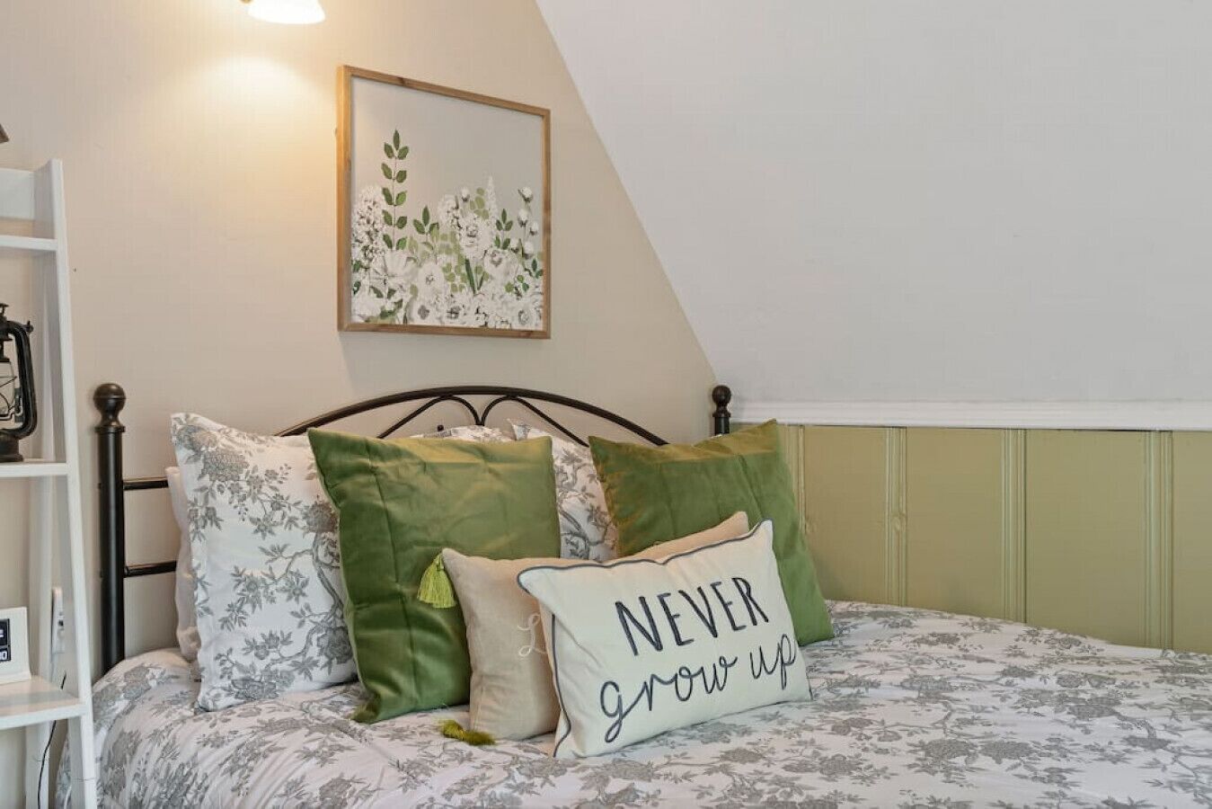 Een slaapkamer met een bed, kussens, een ingelijste afbeelding aan de muur en een plank met spullen.