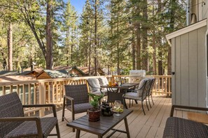 A deck with outdoor furniture, a grill, and a view of a forest. - An amazing cottage that takes you back to childhood tales (Big Bear Lake)