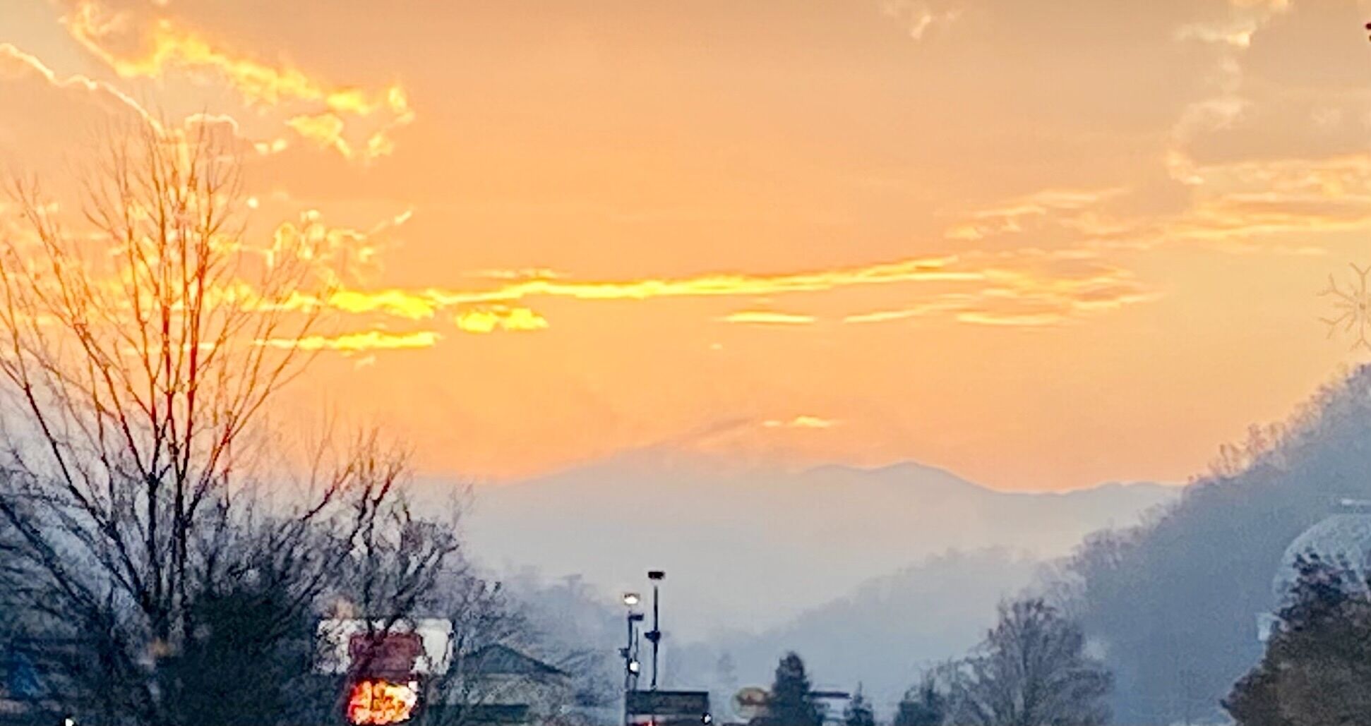 Un atardecer sobre un paisaje montañoso con árboles desnudos y una farola.