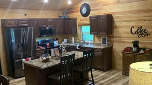 A kitchen with wooden cabinets, a stainless steel refrigerator, a microwave, and a coffee bar area.