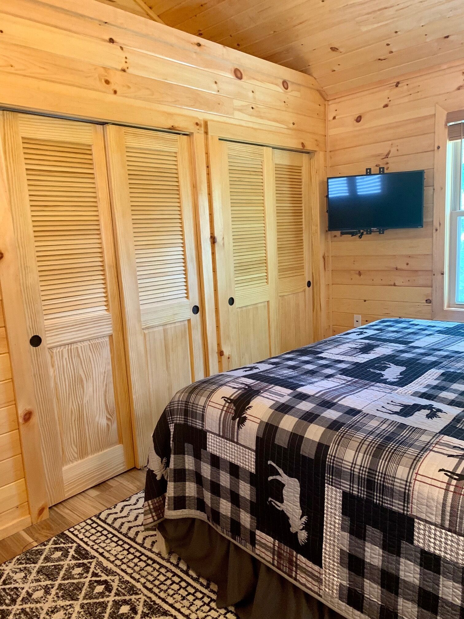 A wooden room with a bed, a television, and a window.