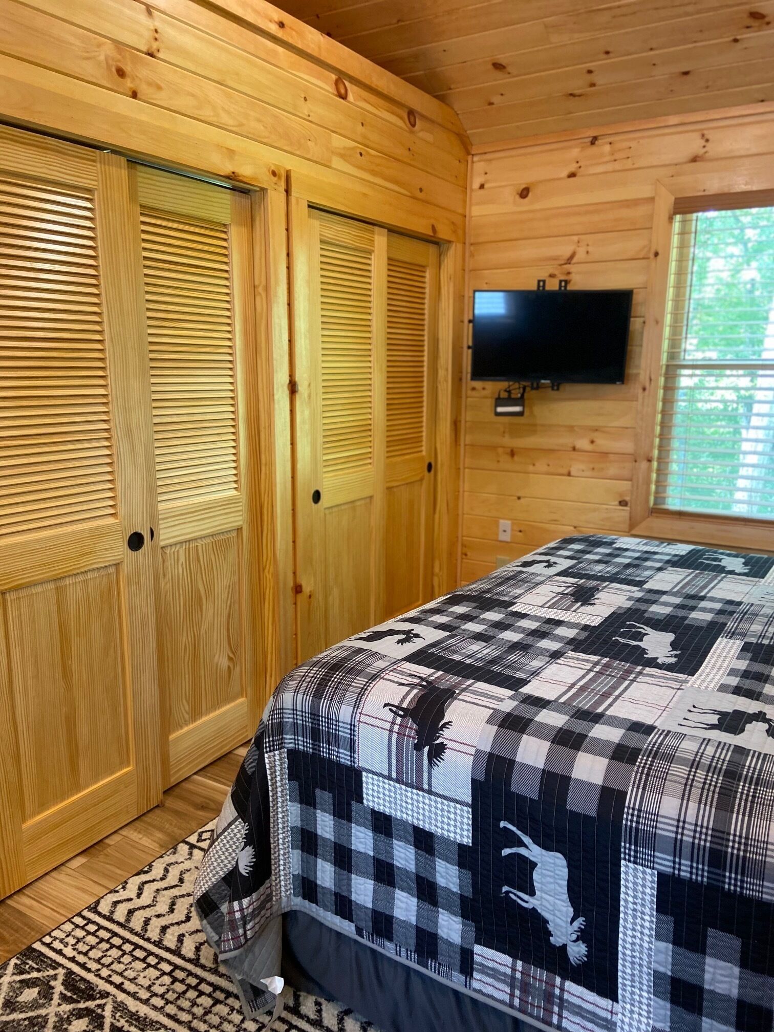 A wooden-paneled room with a bed, a television, and a window.