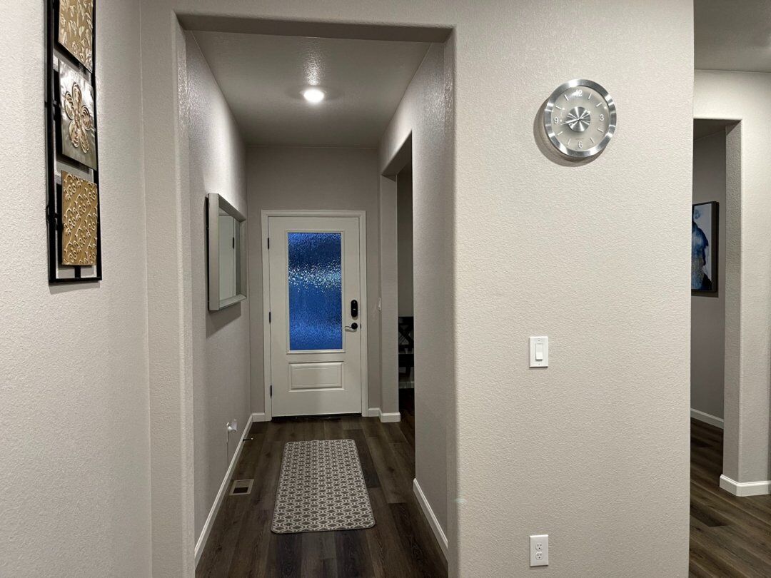 A hallway with a wooden floor, a white door with a frosted glass panel, and a clock on the wall.