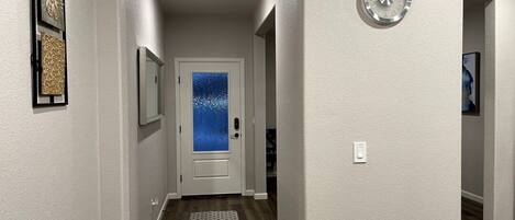 A hallway with a wooden floor, a white door with a frosted glass panel, and a clock on the wall.