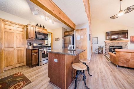 A spacious kitchen with wooden cabinets, a central island with stools, a built-in oven, and a stone fireplace.. Walk to National Park! Mountain Cabin w/ Fireplace
