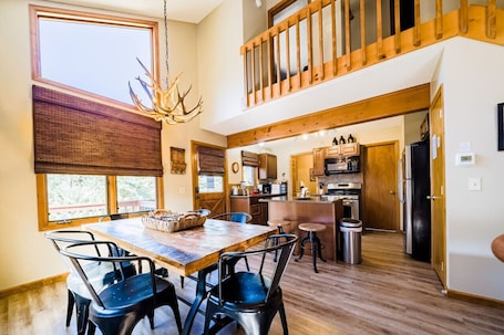 A spacious kitchen with wooden cabinets, a dining area with a large table and chairs, and a view of the outdoors through a window.. Walk to National Park! Mountain Cabin w/ Fireplace