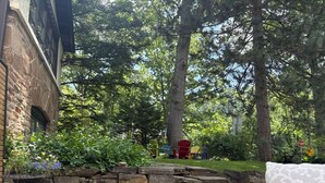 A stone wall with a planter, a gravel path, and a red chair in a garden area. - Port Credit - Mineola Cottage (Mississauga)