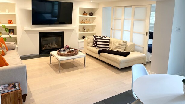 A modern living room with a flat-screen TV, a fireplace, a sofa with patterned cushions, and a coffee table. - Port Credit - Mineola Cottage (Mississauga)
