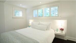 A bedroom with a bed, two bedside tables, a window, and a nightstand with a lamp. - Port Credit - Mineola Cottage (Mississauga)