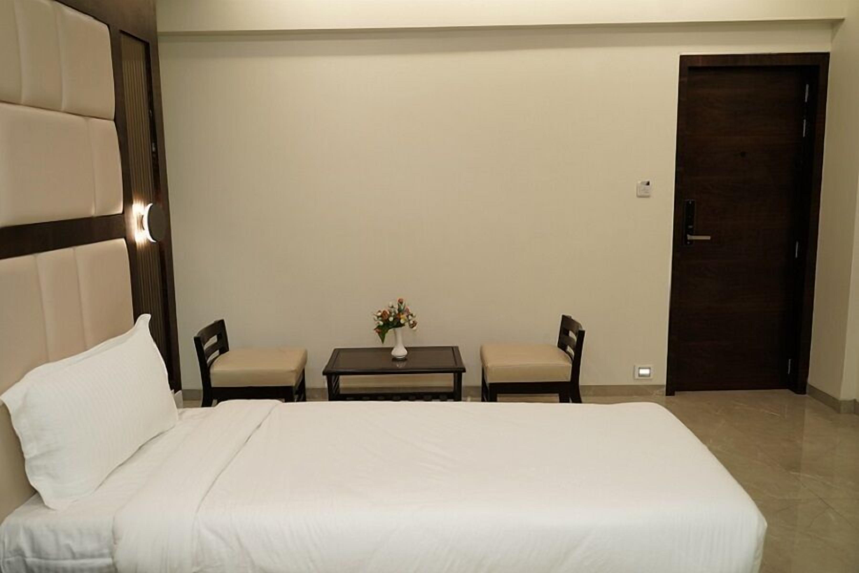 A hotel room with a large bed, two chairs, a small table with a vase of flowers, and a door.