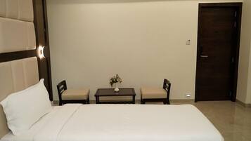 A hotel room with a large bed, two chairs, a small table with a vase of flowers, and a door.