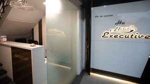 A reception desk with a sign reading "Hotel Naaaz Executive" and a reception area with a staircase leading to an upper level. - Hotel Naaz Executive Near T2 Airport (Mumbai)
