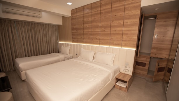 A modern hotel room with a large bed, a smaller bed, a wooden headboard, a bedside table, and a wardrobe. - Hotel Naaz Executive Near T2 Airport (Mumbai)