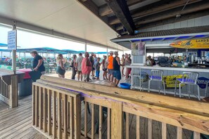 Um deck de madeira com área de bar, assentos externos e vista para o oceano.