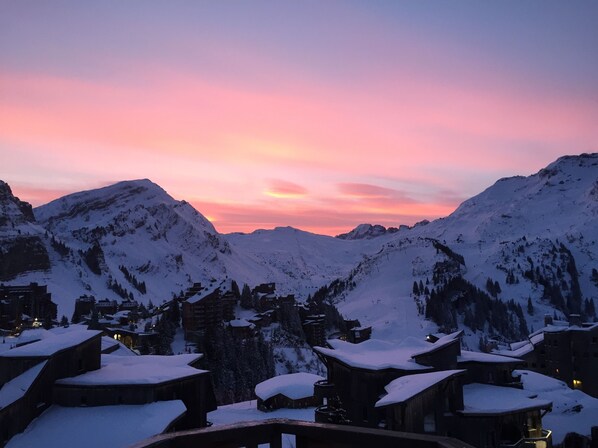 Un village de montagne enneigé, baigné par la lumière du crépuscule, avec des bâtiments en bois et un ciel au coucher du soleil.