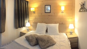 A bedroom with a wooden headboard, two bedside lamps, a framed picture, and a fluffy pillow on the bed.
