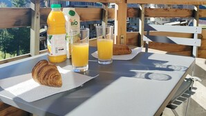 A breakfast setup with a croissant, juice, and a glass on a table with a mountain view.