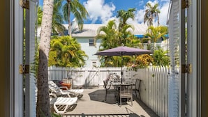 A wooden deck with lounge chairs and a table, surrounded by a white picket fence and palm trees.