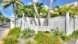 A gated area with a sign for Shipyard Condominiums, surrounded by lush greenery and palm trees.
