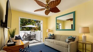A living room with a sofa, a coffee table, a TV, a ceiling fan, a mirror, and a view of a patio with a bicycle.