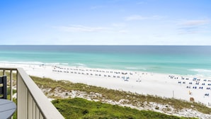 A beach with white sand and clear turquoise water. There are people and umbrellas on the beach.